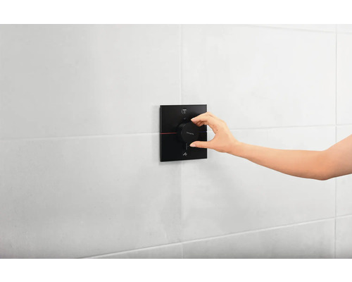 Une main actionne un mitigeur thermostatique pour douche ou baignoire sur un mur carrelé