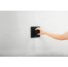 Eine Hand bedient einen schwarzen Duschthermostat an einer weißen Wand.