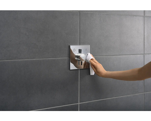 Une main nettoie un mitigeur de douche avec un chiffon