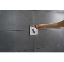 Gros plan d''une main actionnant un mitigeur de douche sur un mur carrelé