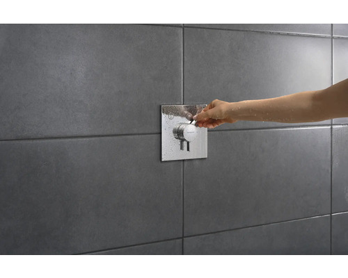 Gros plan d''une main actionnant un mitigeur de douche sur un mur carrelé