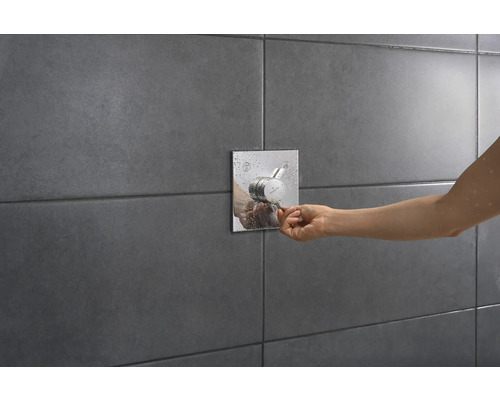 Thermostat de douche apparent avec manipulation par une personne sur un mur carrelé