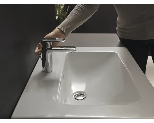 Aufnahme eines Waschbeckens mit Wasserhahn in einem Badezimmer, die eine Hand zeigt, die den Wasserhahn bedient