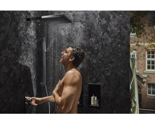 Homme sous une douche à effet pluie dans une salle de bains moderne avec des carreaux de marbre foncé