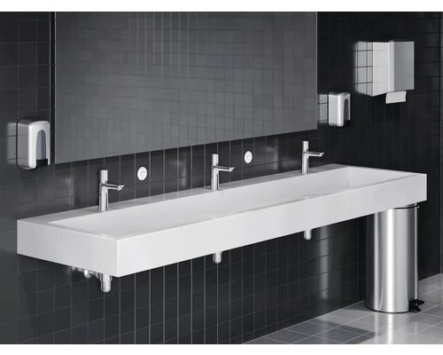 Badezimmer mit langem Waschbecken, Armaturen, Seifenspender, Papiertuchspender, Spiegel und Mülleimer