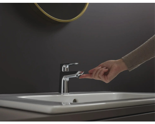 Robinet de lavabo avec un doigt sur le bouton de commande dans une salle de bains.