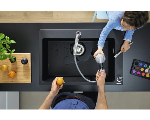 Vue de dessus d''un évier noir avec robinetterie et d''une personne lavant des fruits pendant qu''un enfant peint