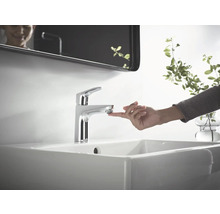 Waschtischarmatur aus Metall auf einem Waschbecken mit einer Hand, die den Wasserhahn berührt