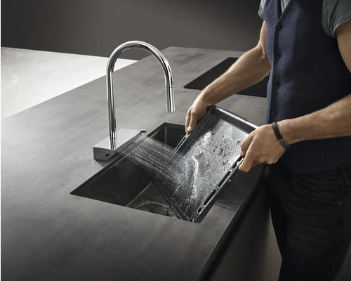 Mann spült Backblech in einer Küchenspüle mit Wasserhahn.