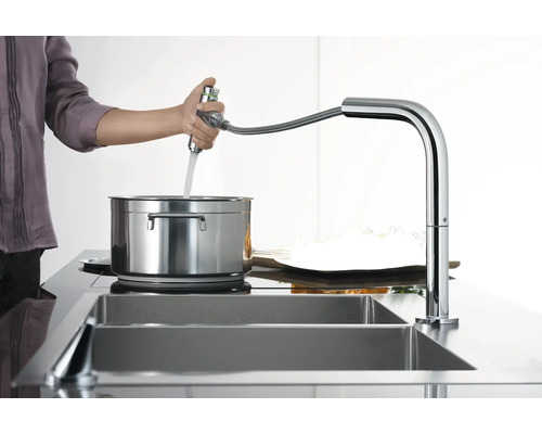 Person befüllt Topf mit Wasserhahn in Chromoptik an Spüle