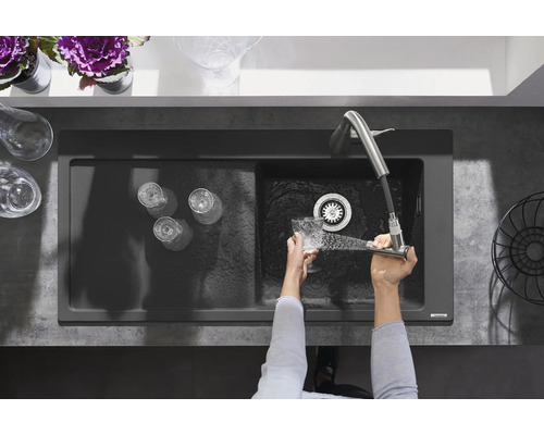 Draufsicht auf eine Spüle mit Abtropffläche, Gläsern und einer Person, die ein Glas unter einem Wasserhahn abspült.