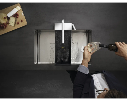 Évier en acier inoxydable avec accessoires et une personne versant un verre de vin.