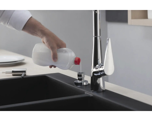 Une personne remplit du liquide vaisselle dans un distributeur de savon à côté d''un évier et d''un robinet.