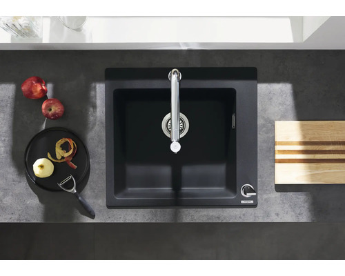 Évier de cuisine avec robinet, planche à découper, pommes et éplucheur sur un plan de travail.