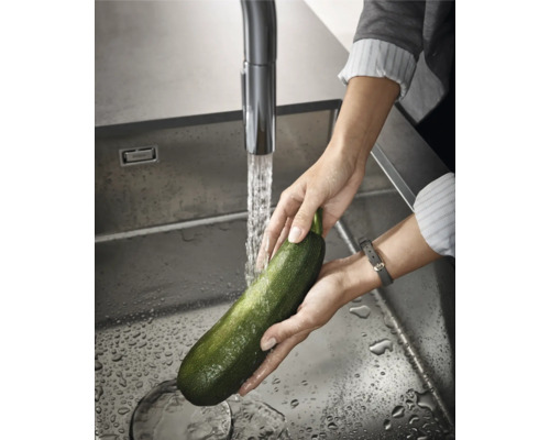 Eine Zucchini wird unter einem Wasserhahn in einer Spüle gewaschen.