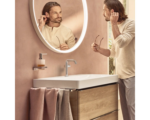 Modernes Badezimmer mit Waschbecken, Armatur, beleuchtetem Spiegel und einem Mann, der sich im Spiegel betrachtet