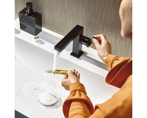 Waschbeckenarmatur mit eckigem Auslauf, eine Person wäscht einen Kamm unter fließendem Wasser