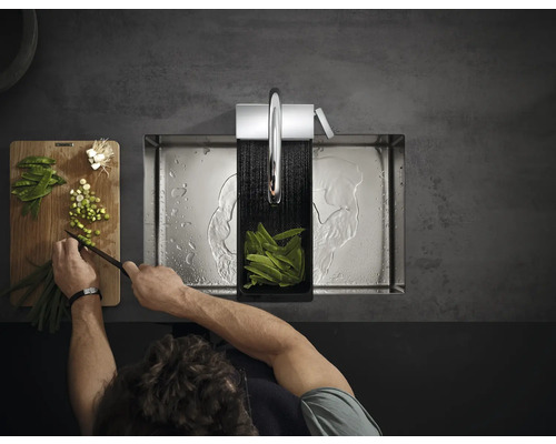 Eine Person bereitet in einer Edelstahlspüle Gemüse zu, während Wasser aus einem Wasserhahn läuft.