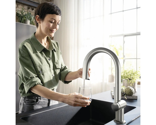 Frau füllt Wasser in ein Glas unter einem Küchenarmatur