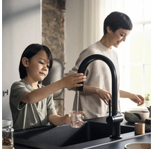Un enfant remplit un verre d''eau à partir d''un robinet de cuisine noir