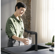 Femme remplit un verre au robinet dans une cuisine moderne.