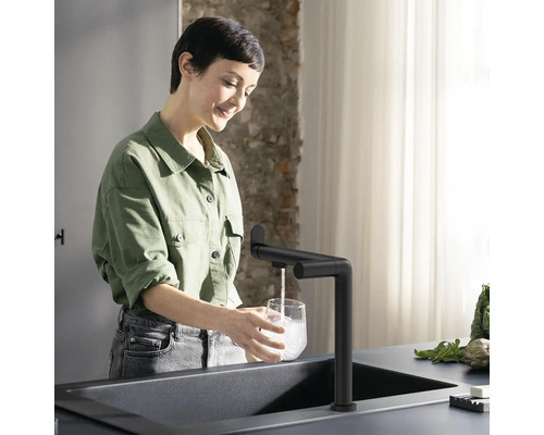 Femme remplit un verre au robinet dans une cuisine moderne.