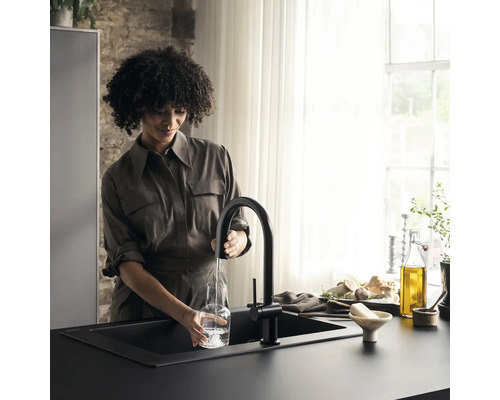 Frau füllt Wasser in eine Glasflasche am schwarzen Spültisch mit Küchenarmatur.