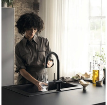 Une femme remplit une bouteille en verre d''eau à un robinet noir dans une cuisine.