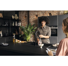 Cuisine claire avec une femme remplissant une bouteille d''eau et une autre femme lisant un magazine.