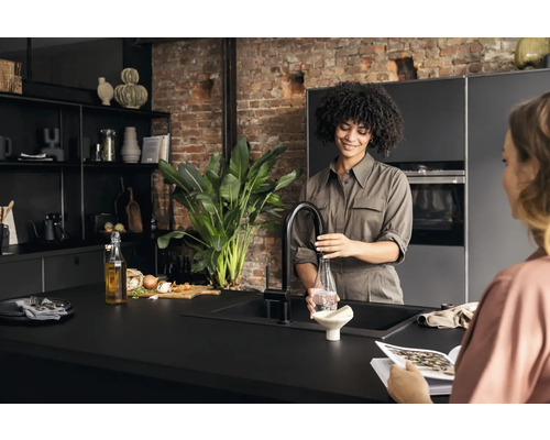 Helle Küche mit einer Frau, die eine Flasche mit Wasser befüllt, und einer weiteren Frau, die eine Zeitschrift liest.