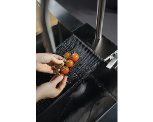 Person wäscht Kirschtomaten unter einem Wasserstrahl im Spülbecken mit Hansgrohe Logo