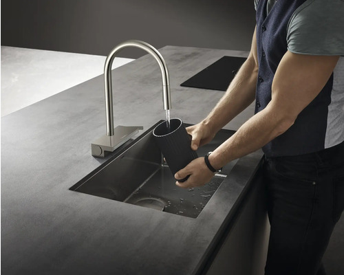 Edelstahlspüle mit Wasserhahn und Person, die ein Gefäß hält
