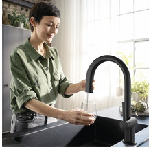 Femme remplissant un verre d''eau sous un robinet noir dans une cuisine