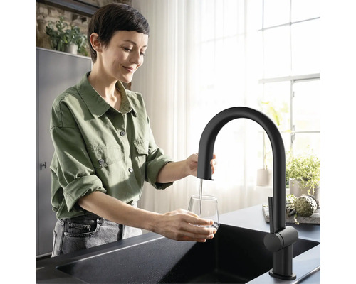 Frau füllt Wasser in ein Glas unter einem schwarzen Wasserhahn in einer Küchenspüle.
