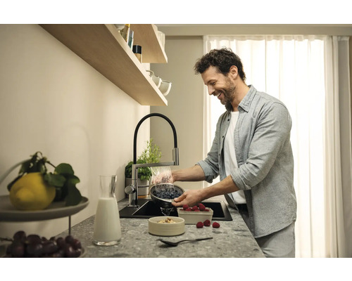 Un homme lave des baies dans un évier de cuisine avec un robinet de cuisine.