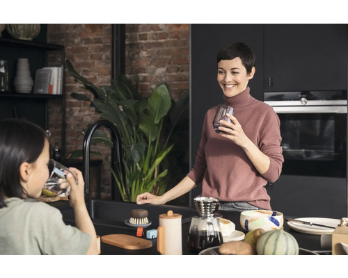 Helle Küche mit Mutter und Kind an der Spüle, ausgestattet mit Armatur, Spülbürste und Geschirr