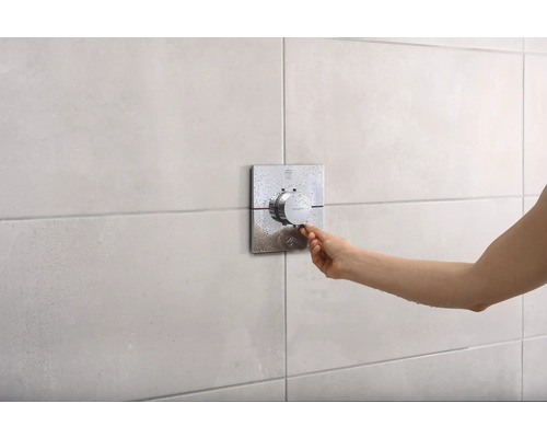 Une main actionne un mitigeur de douche avec un régulateur de température sur un mur carrelé