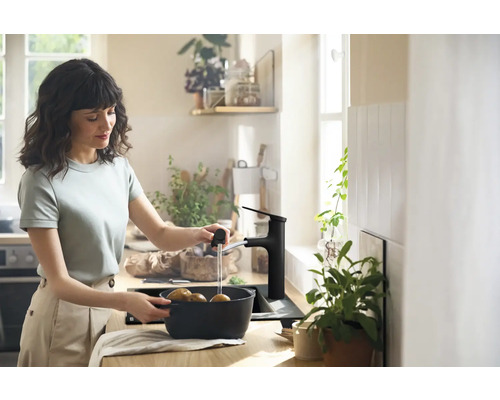 Frau wäscht Kartoffeln in einer Küchenspüle mit schwarzer Armatur