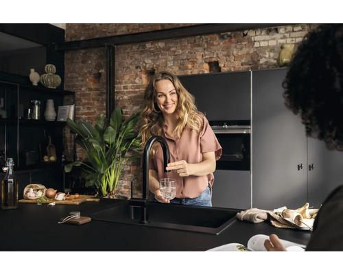 Frau füllt Wasserhahnwasser in Glas in moderner Küche