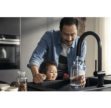 Vater und Kind befüllen eine Glasvase mit Wasser aus einem schwarzen Küchenarmatur