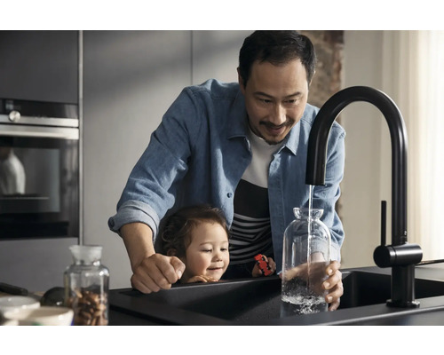 Vater und Kind befüllen eine Glasvase mit Wasser aus einem schwarzen Küchenarmatur