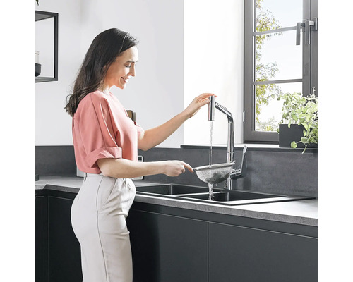 Frau spült Lebensmittel im Küchensieb unter einem Wasserhahn in einer modernen Küche.