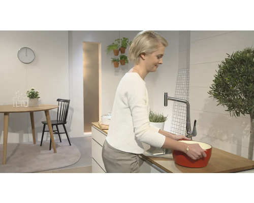 Eine Frau steht in einer hellen Küche und spült eine rote Schüssel unter einem Wasserhahn.