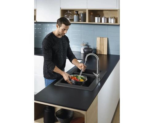 Un homme lave des légumes dans un évier de cuisine avec un robinet.