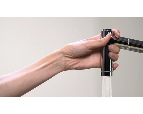 Eine Hand betätigt einen verchromten Wasserhahn, aus dem Wasser fließt.