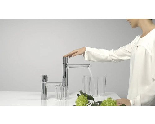 Frau betätigt einen Wasserhahn mit fließendem Wasser in ein Glas