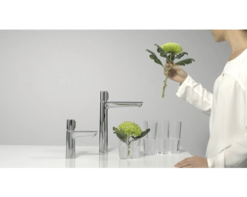 Zwei verchromte Wasserhähne neben Blumen und Gläsern auf einer Arbeitsfläche.