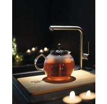 Théière avec thé, robinet et planche à découper dans une scène de cuisine sombre.