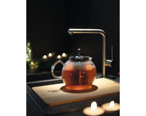 Théière avec thé, robinet et planche à découper dans une scène de cuisine sombre.