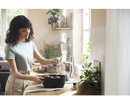 Femme lavant des pommes de terre dans une cuisine avec un robinet.